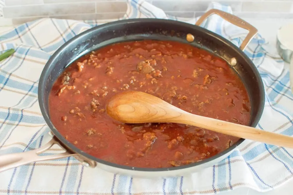 Mixing meat and tomato sauce in a large skillet with a wooden spoon