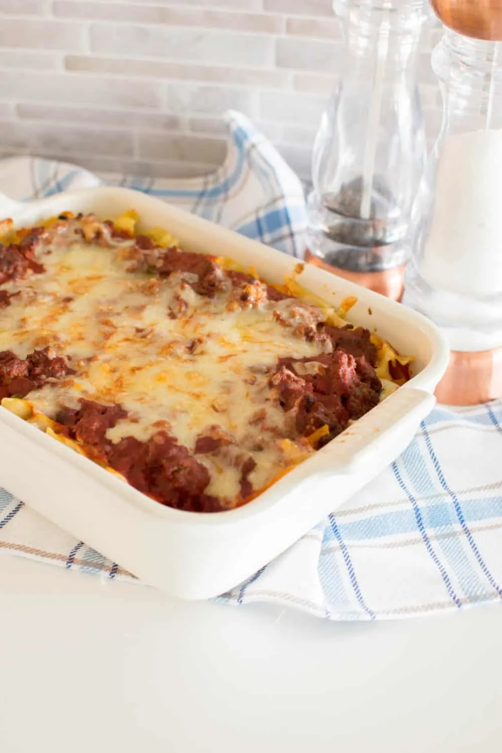Sour cream noodle bake in a white casserole dish and a blue plaid towel in the background