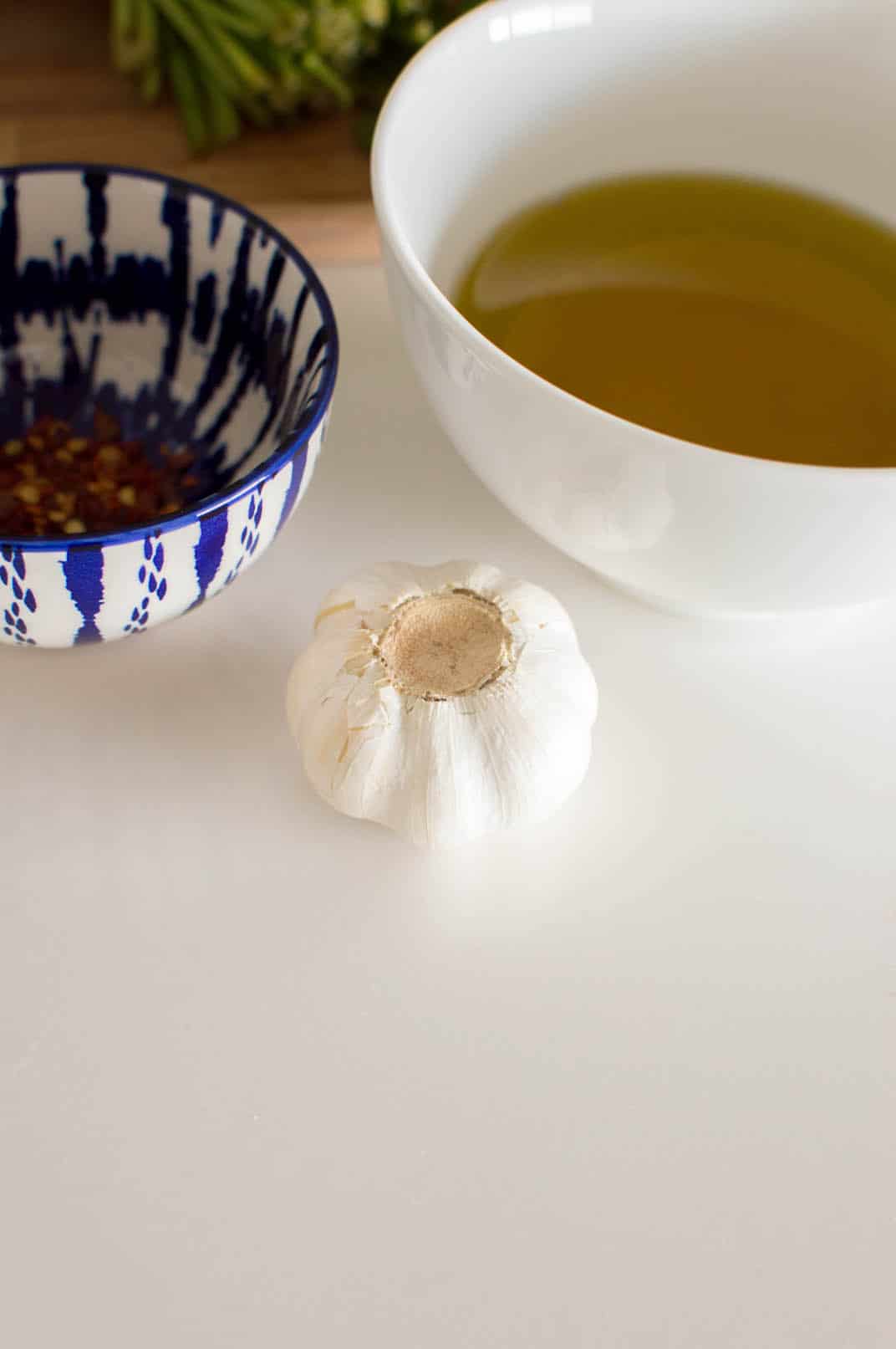 A whole garlic on a white table surrounded by bowls of various ingredients to make easy chimichurri sauce