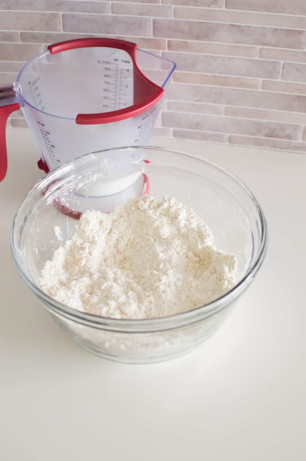 Butter cut into a bowl of dry ingredients, with a liquid measuring cup in the background