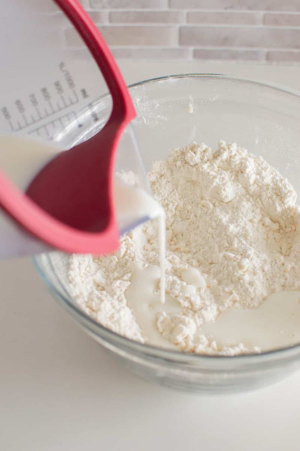 Pouring buttermilk into a glass bowl of dry ingredients