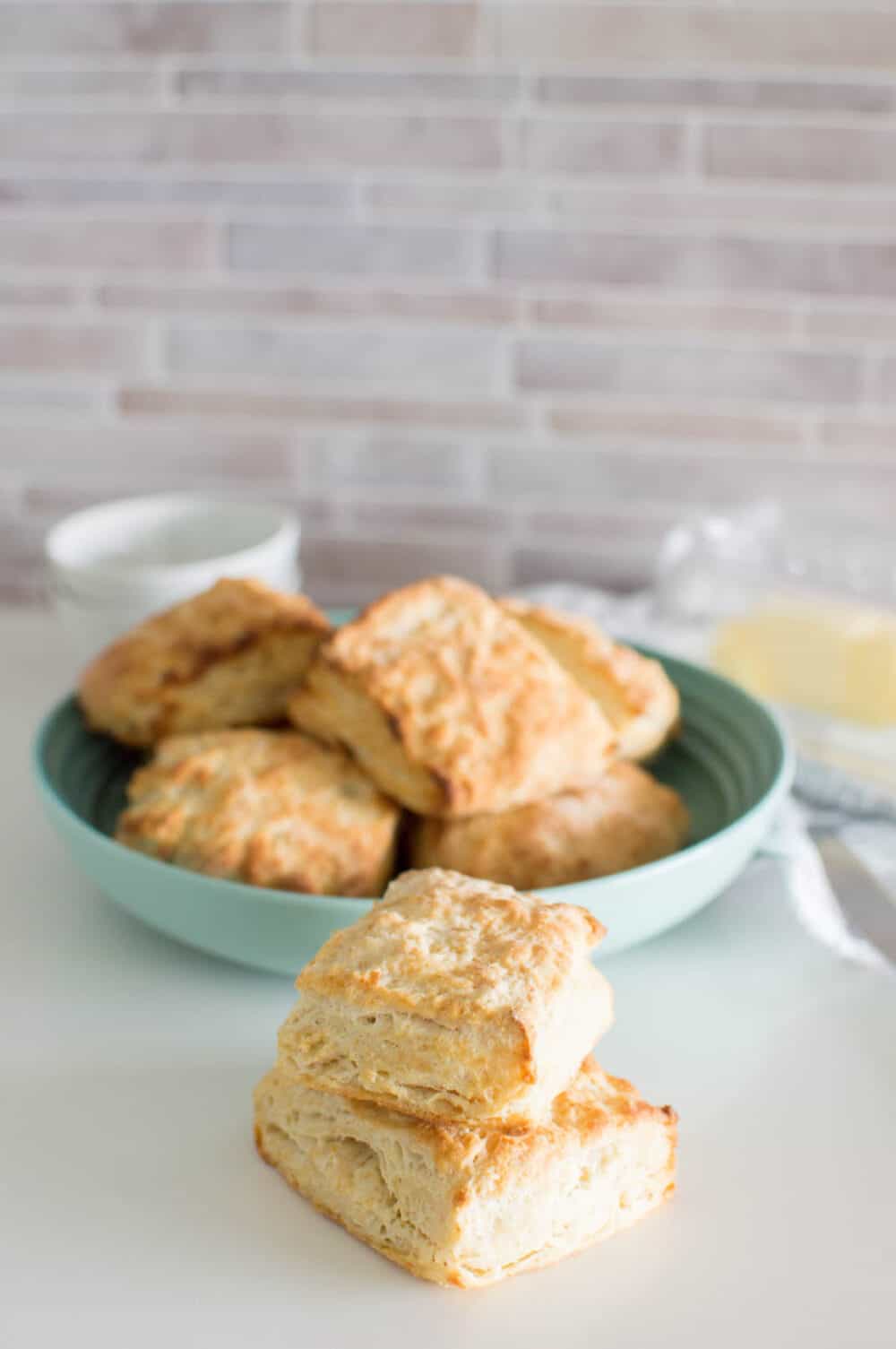 Two homemade biscuits stacked on each other with a bowl full of biscuits in the background