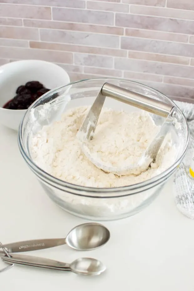 A pastry cutter cutting into a large bowl of flour and butter to make Cherry Almond Scones.