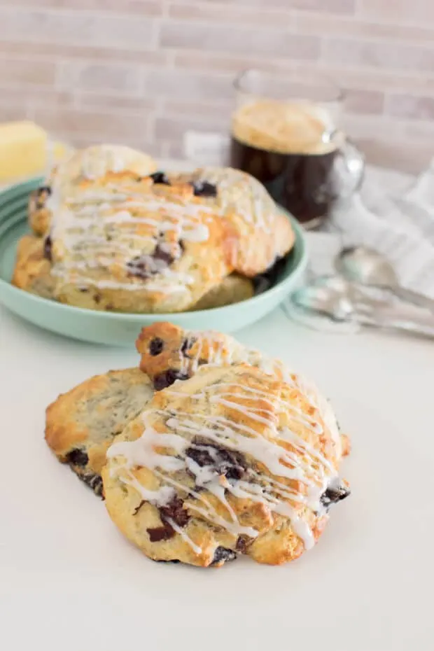 A stack of three cherry almond scones with a bowl of scones in the background, along with a mug of coffee and measuring spoons