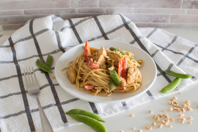 Peanut butter noodles with chicken and vegetables in a white bowl
