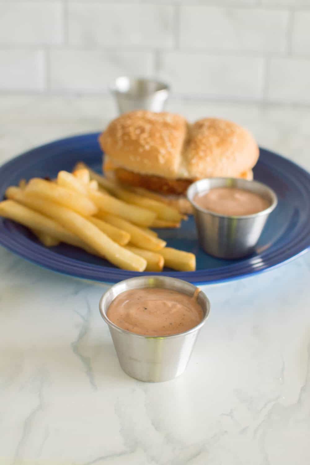 Homemade Guthrie’s Sauce in a small, silver bowl with a chicken burger and French fries on a blue plate in the background