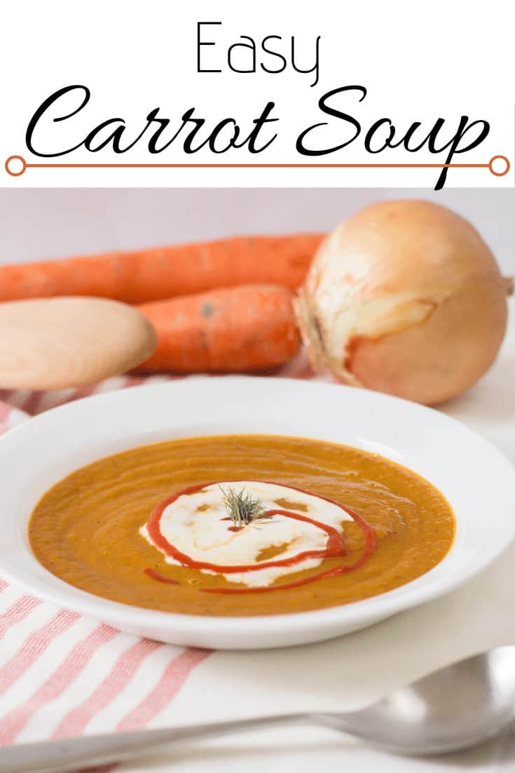 Carrot soup in a white bowl with onions, carrots and a wooden spoon in the background