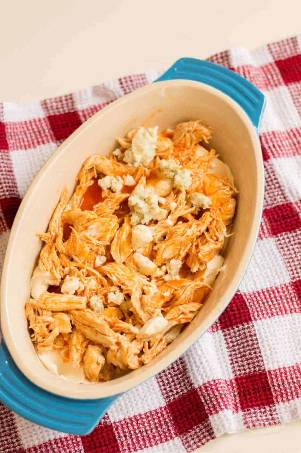 Layering chicken, cream cheese, and other ingredients for buffalo chicken dip appetizer