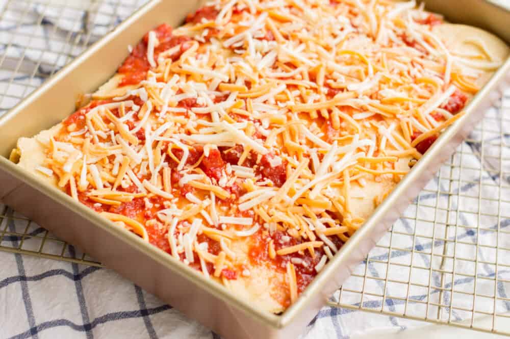 adding grated cheese on top of chicken enchilada casserole
