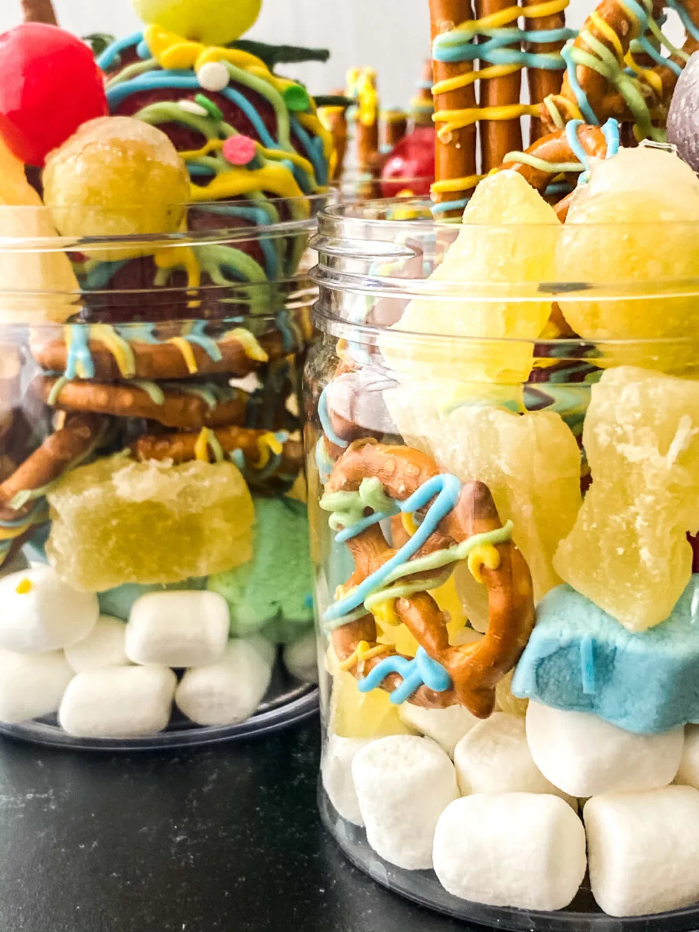 Close up of sweet charcuterie jars with marshmallows, dried fruit, Tanghulu fruit and chocolate striped pretzels.