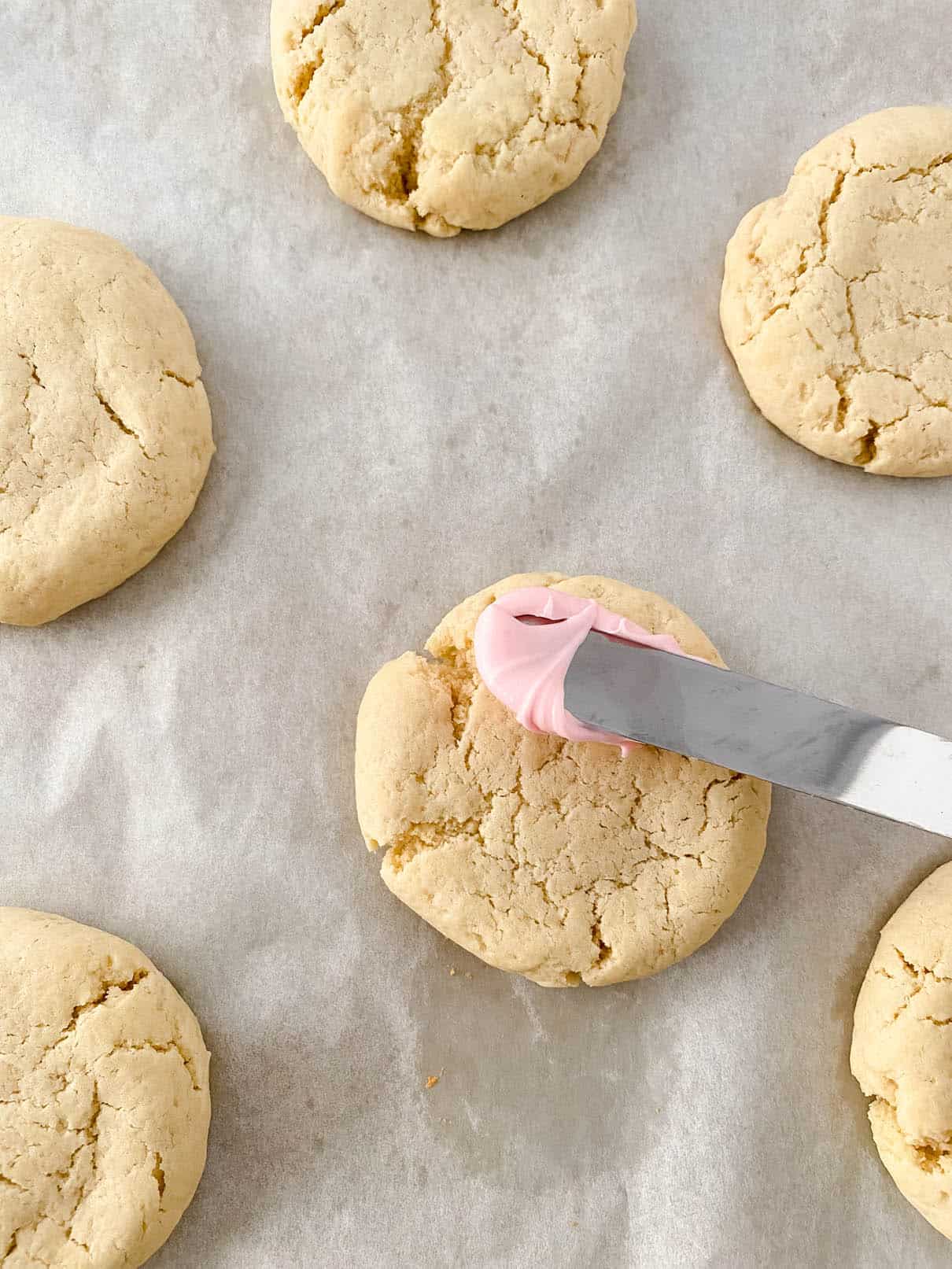 Frosting sugar cookies with pink almond buttercream using an offset spatula