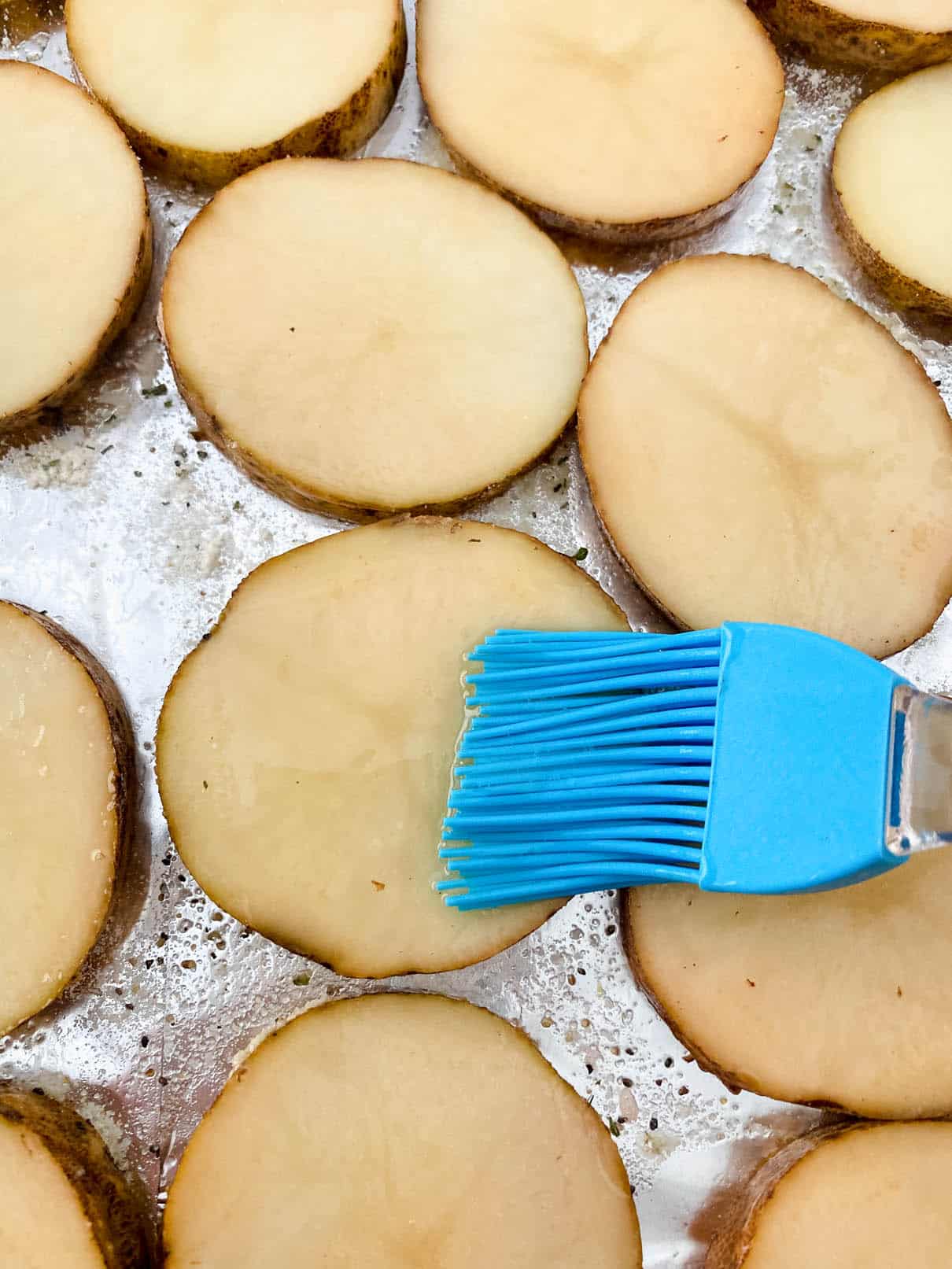Brushing olive oil on sliced potatoes with a blue pastry brush