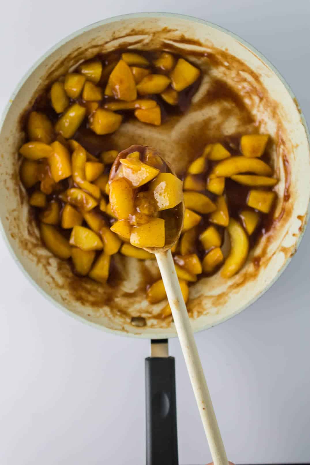 Cooking peach filling for Peach Cobbler Egg Rolls and stirring with a wooden spoon