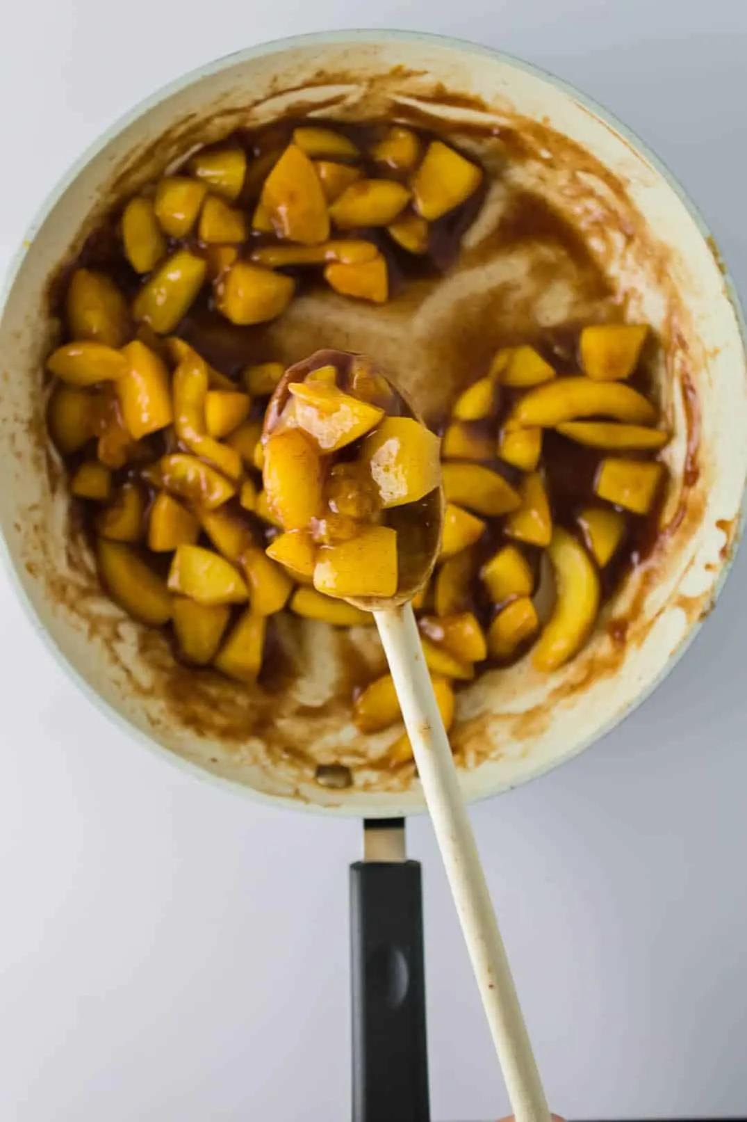 Cooking peach filling for Peach Cobbler Egg Rolls and stirring with a wooden spoon