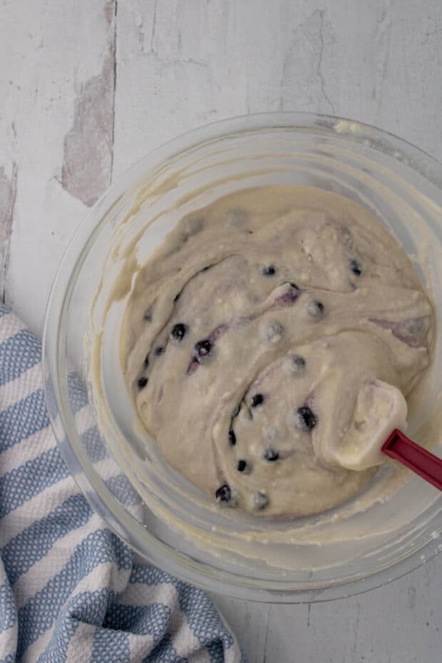 Mixing blueberry muffin batter in a glass bowl with a spatula