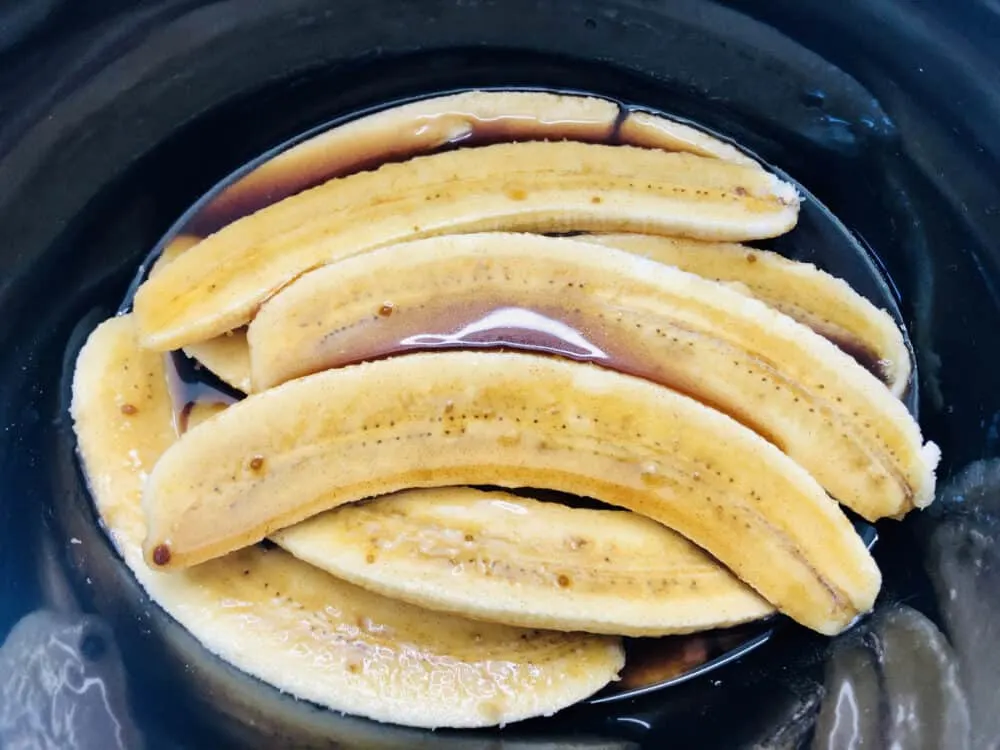 Halved bananas in a slow cooker with sugar and butter sauce