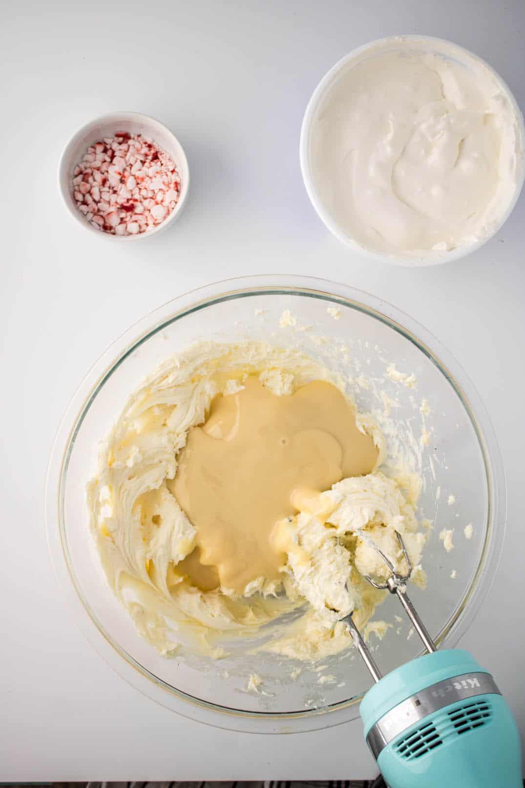 Adding condensed milk to a mix of soft cream and cookie sandwich fillings, mixed in a glass bowl.