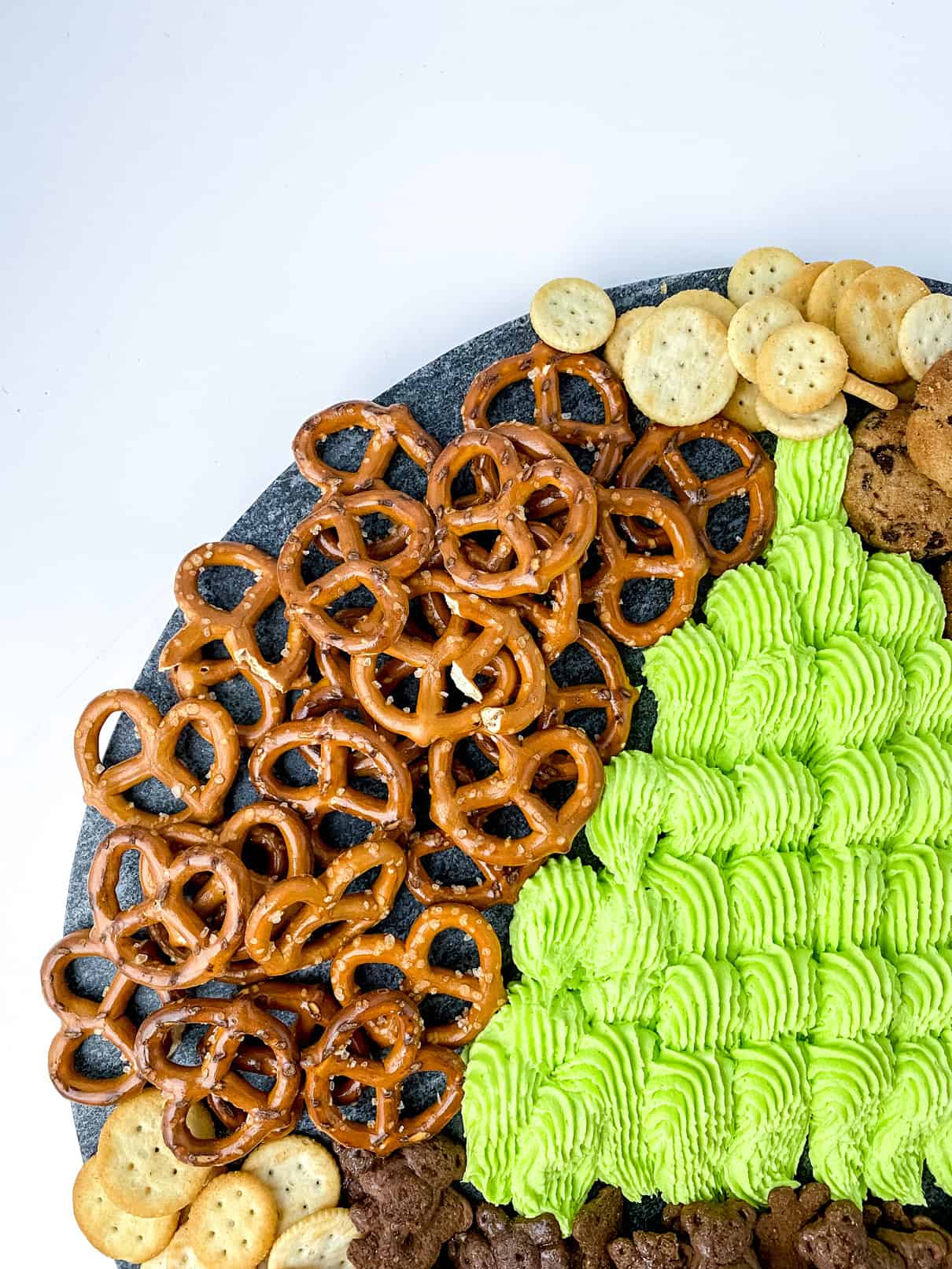 Partial view of a Holiday Frosting Board, comprised of green buttercream, cookies, pretzels and crackers