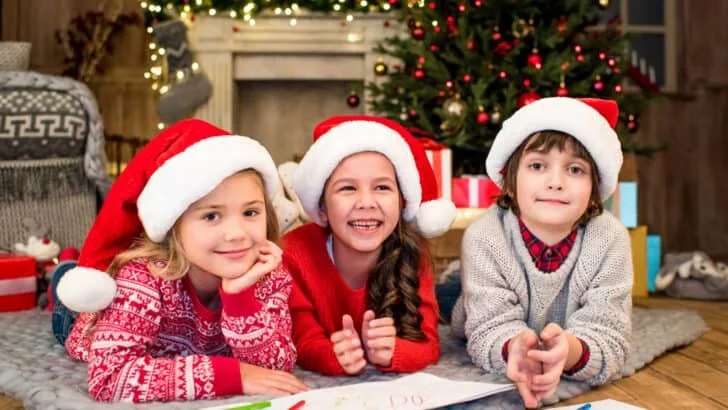 Three children in santa hats drawing on paper with markers