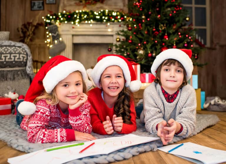 Three children in santa hats drawing on paper with markers