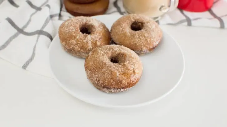 3 homemade gingerbread donuts on a white plate with more donuts in the background