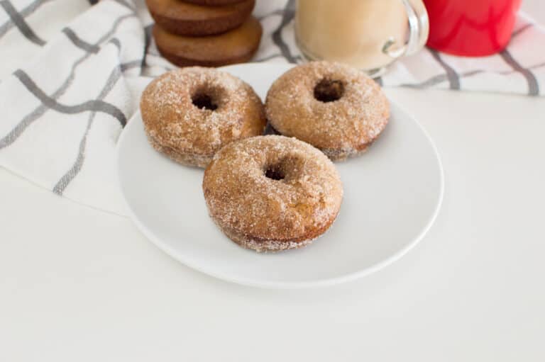 3 homemade gingerbread donuts on a white plate with more donuts in the background