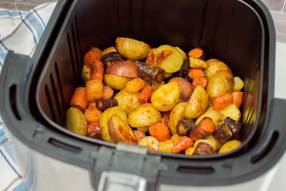 Potatoes and carrots coated with oil and seasoning, laying in an air fryer basket