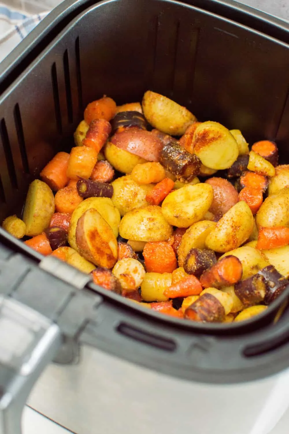 Potatoes and carrots coated with oil and seasoning, laying in an air fryer basket