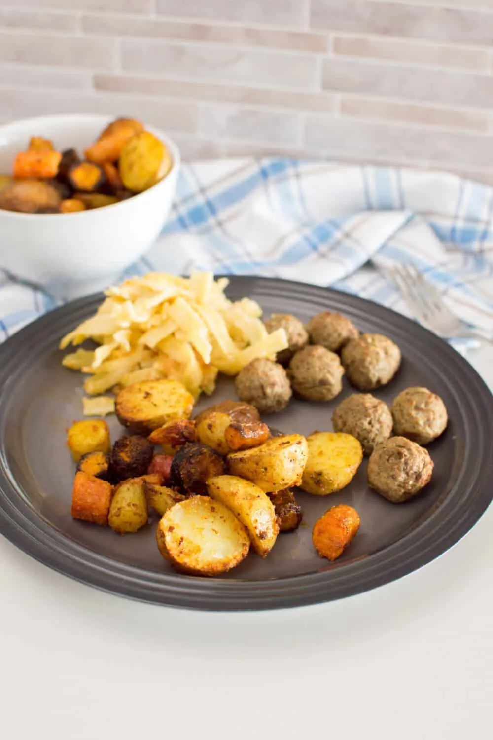 Roasted air fryer potatoes and carrots served on a grey plate with meatballs and pasta