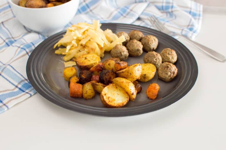 Roasted air fryer potatoes and carrots served on a grey plate with meatballs and pasta
