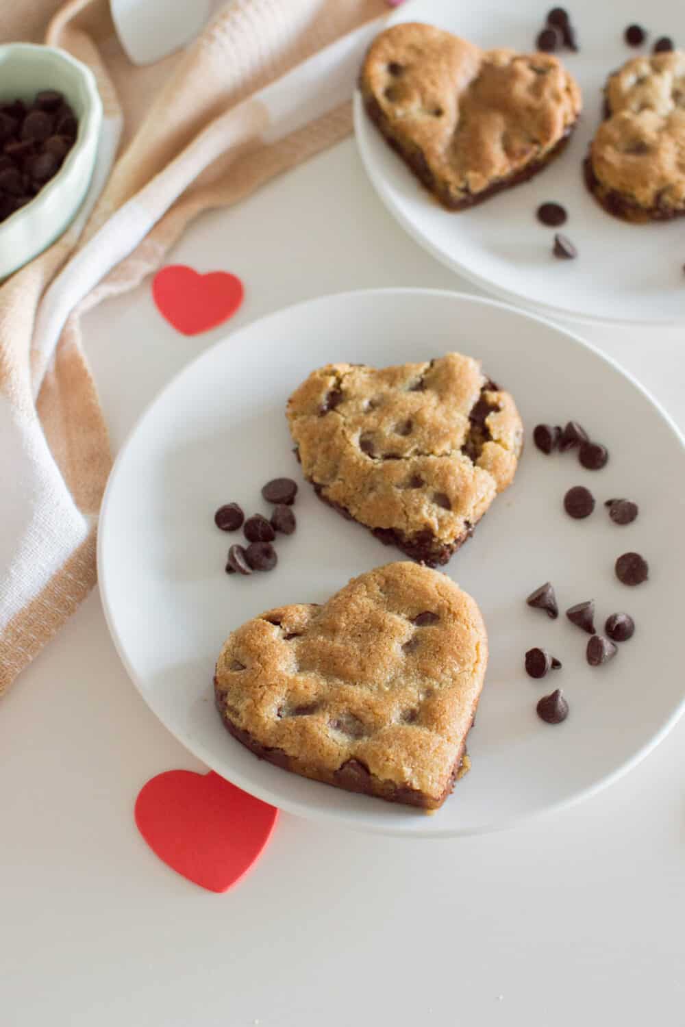 Heart-shaped chocolate chip cookies on a white plate, surrounded by chocolate chips