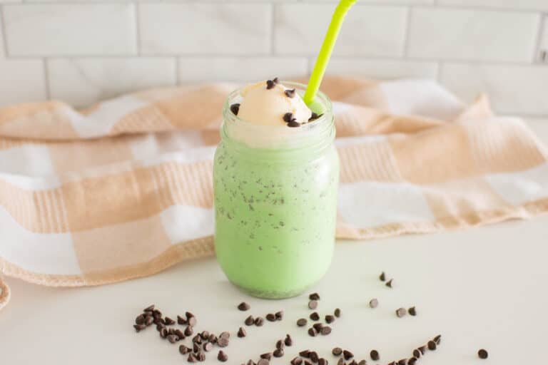 Mint Chocolate Chip Milkshake in a mason jar surrounded by chocolate chips and a plaid tea towel