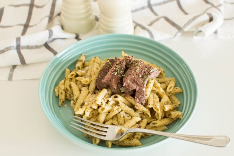 Homemade pesto pasta steak in a green pasta bowl with a fork, topped with medium rare steak