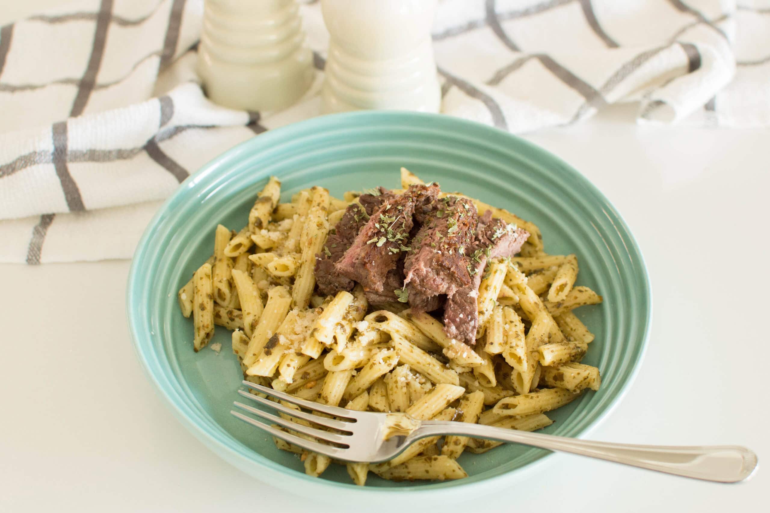 Homemade pesto pasta steak in a green pasta bowl with a fork, topped with medium rare steak