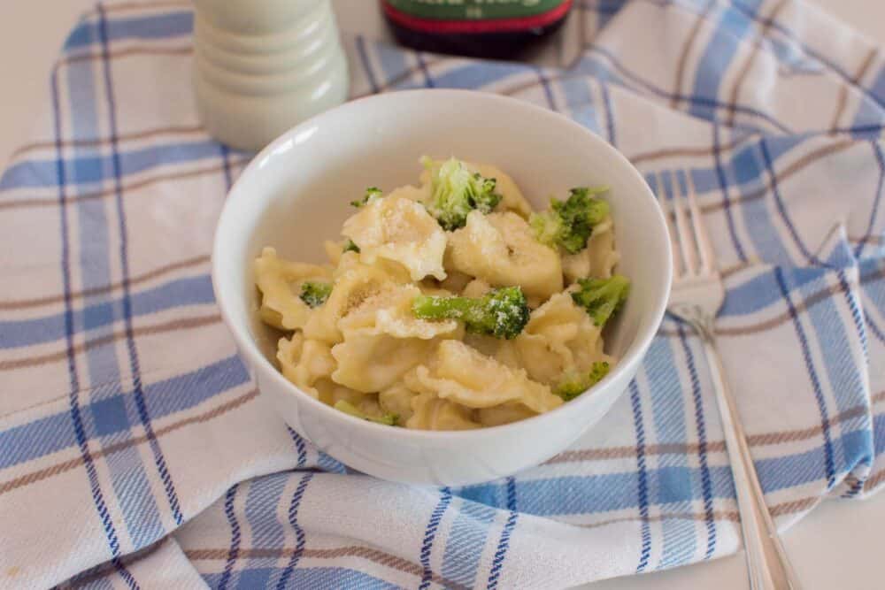 Close-up of a bowl of homemade alfredo tortellini with homemade sauce, sitting on a plaid napkin