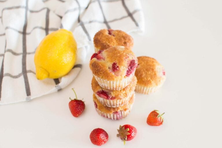 A stack of Strawberry and Lemon Muffins on a white table, surrounded by strawberries