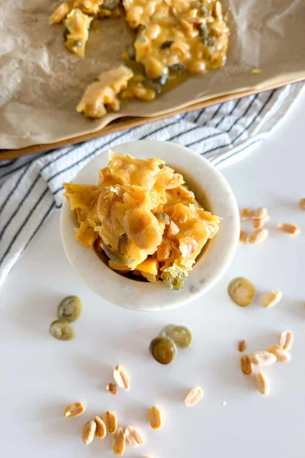 Bird's eye view of Jalapeno Peanut Brittle sitting in a marble bowl on a white table surrounded by additional pieces of peanut brittle and jalapeno