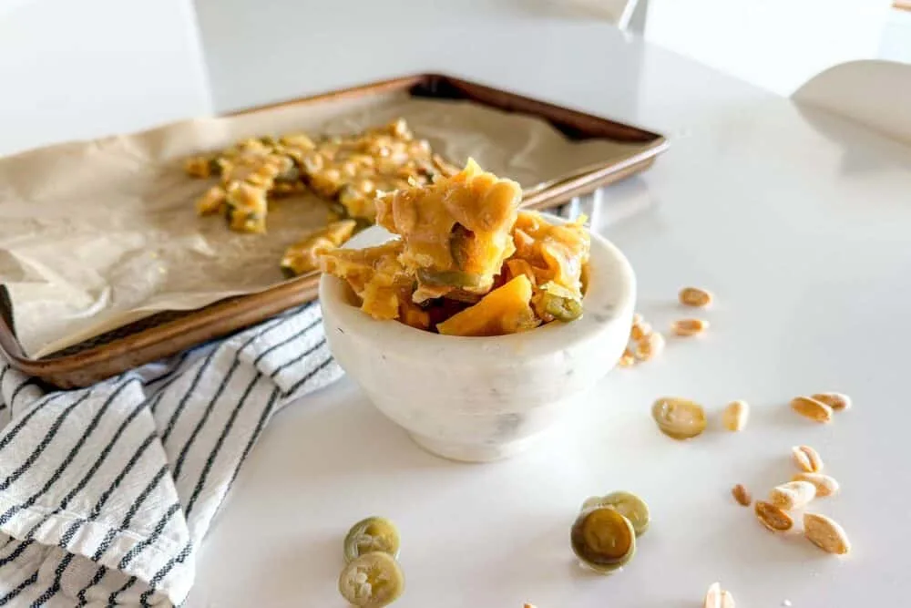 Jalapeno Peanut Brittle sitting in a marble bowl on a white table surrounded by additional pieces of peanut brittle and jalapeno