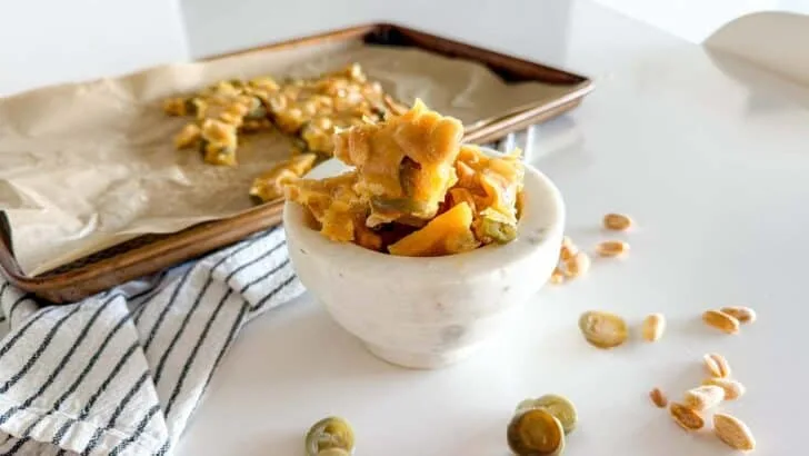 Jalapeno Peanut Brittle sitting in a marble bowl on a white table surrounded by additional pieces of peanut brittle and jalapeno
