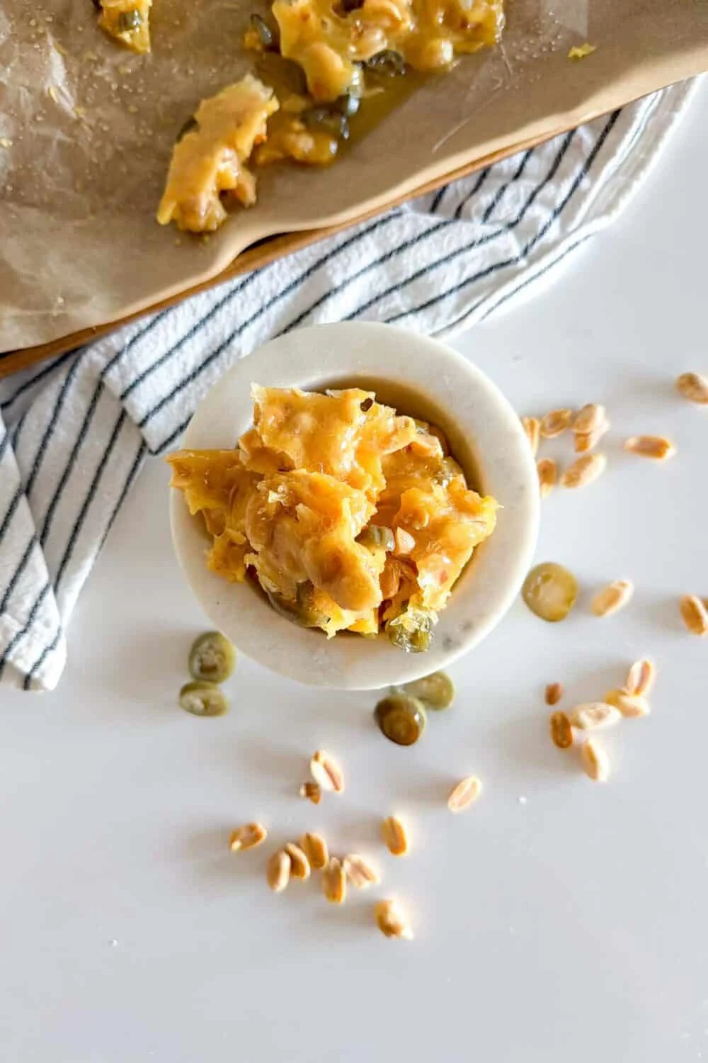 Top view of Jalapeno Peanut Brittle sitting in a marble bowl on a white table surrounded by additional pieces of peanut brittle and jalapeno