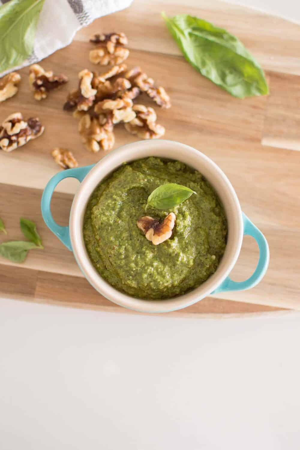 Jar of pesto sauce topped with fresh basil and walnuts