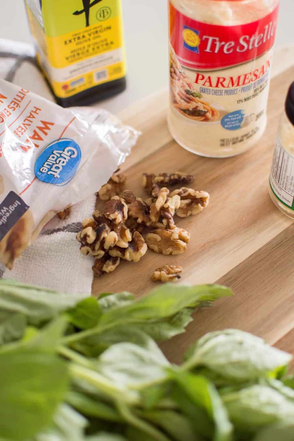 Walnuts and garlic beside jars of oil and parmesan, prepped for pesto