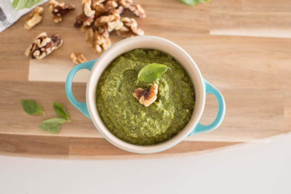 Close-up of smooth green pesto garnished with walnuts and basil