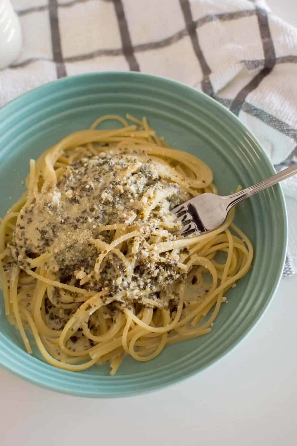 Bird's eye view of Alfredo Pesto Pasta served in a green dish on a tea towel