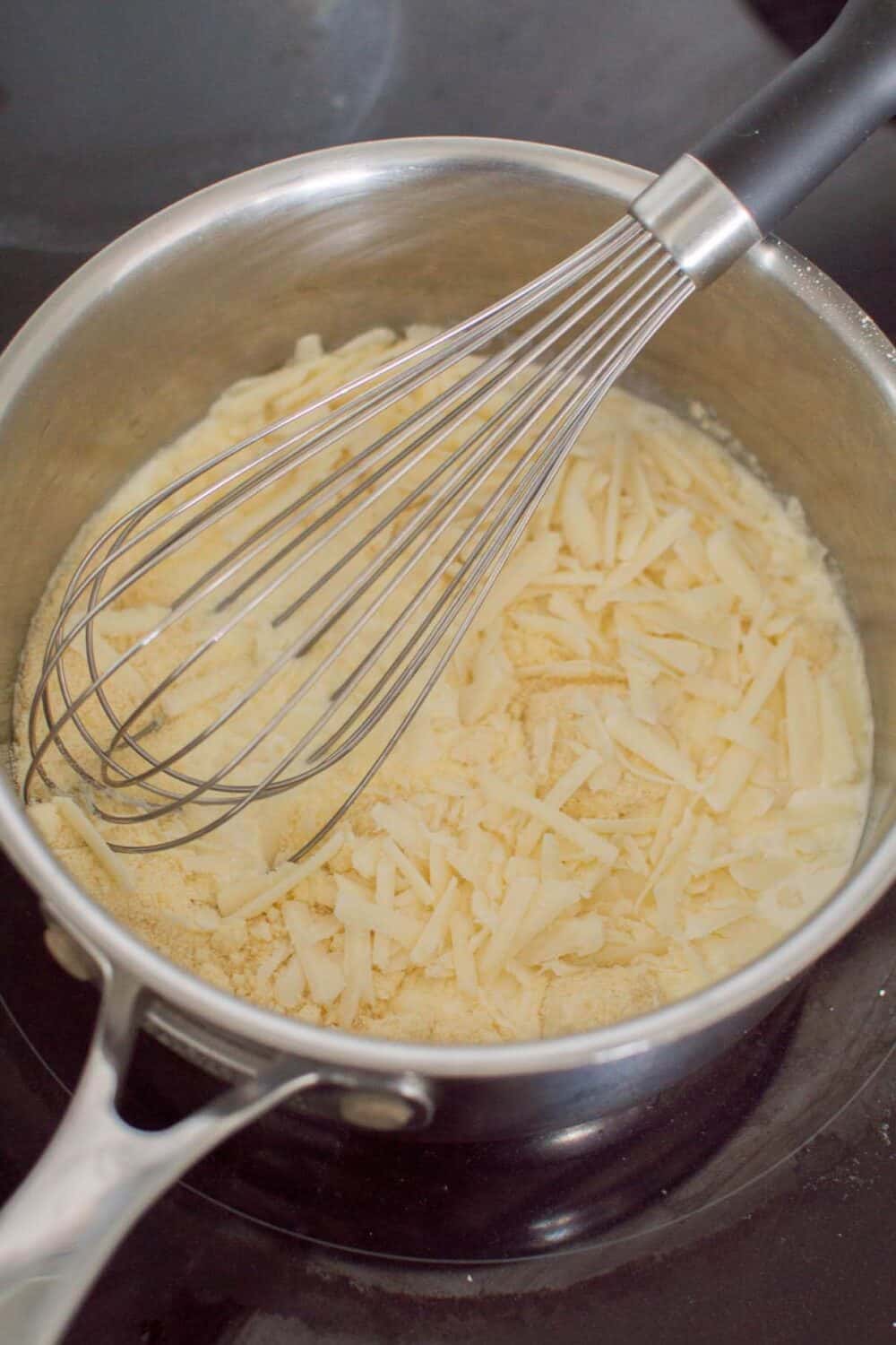 Melting cheese into cream in a small sauce pan to make Alfredo Pesto Pasta