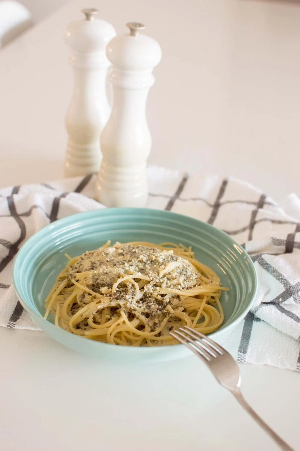 Alfredo Pesto Pasta served in a green dish on a tea towel with a fork