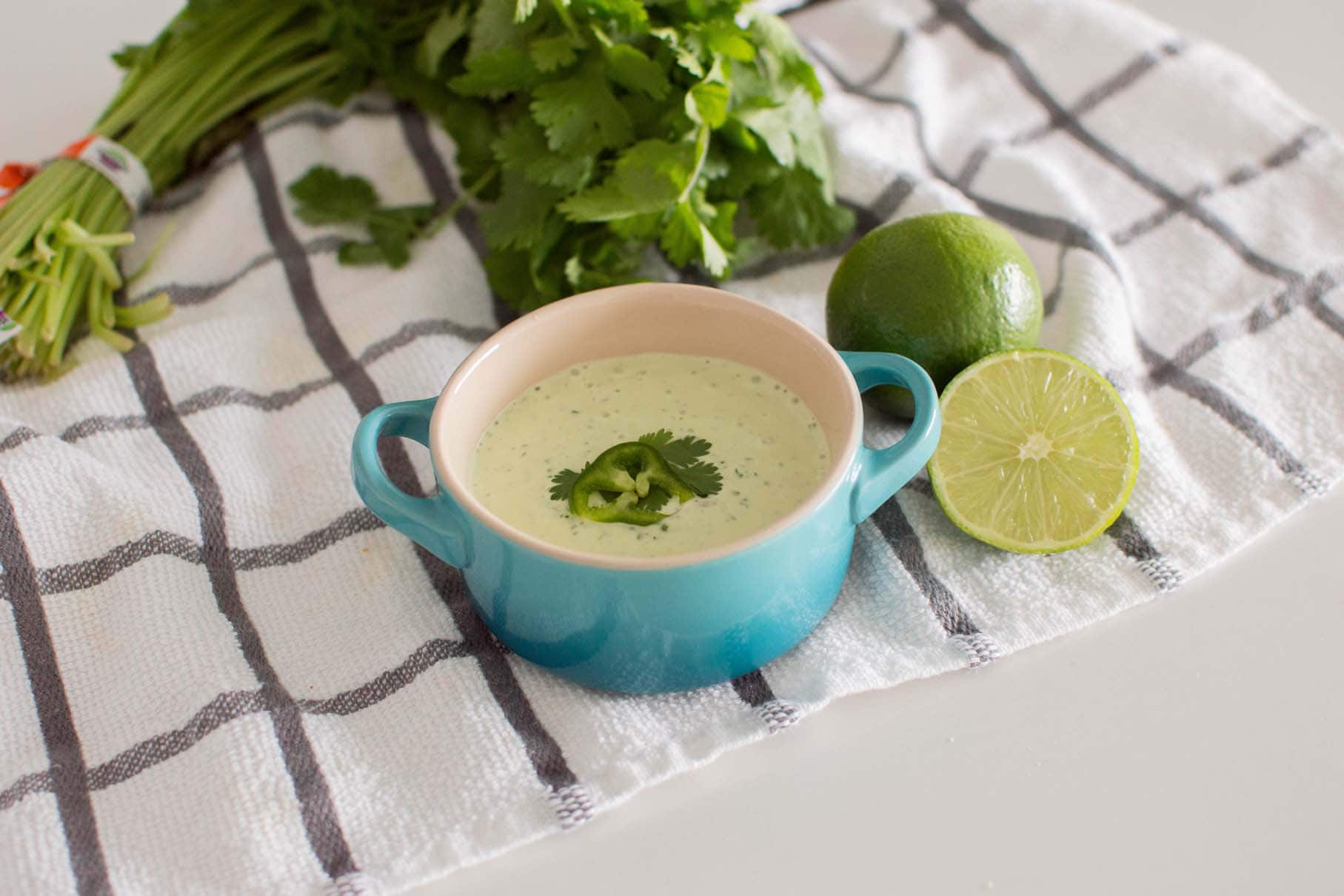Easy Jalapeno Aioli Recipe served in a blue serving dish, surrounded by limes and fresh cilantro