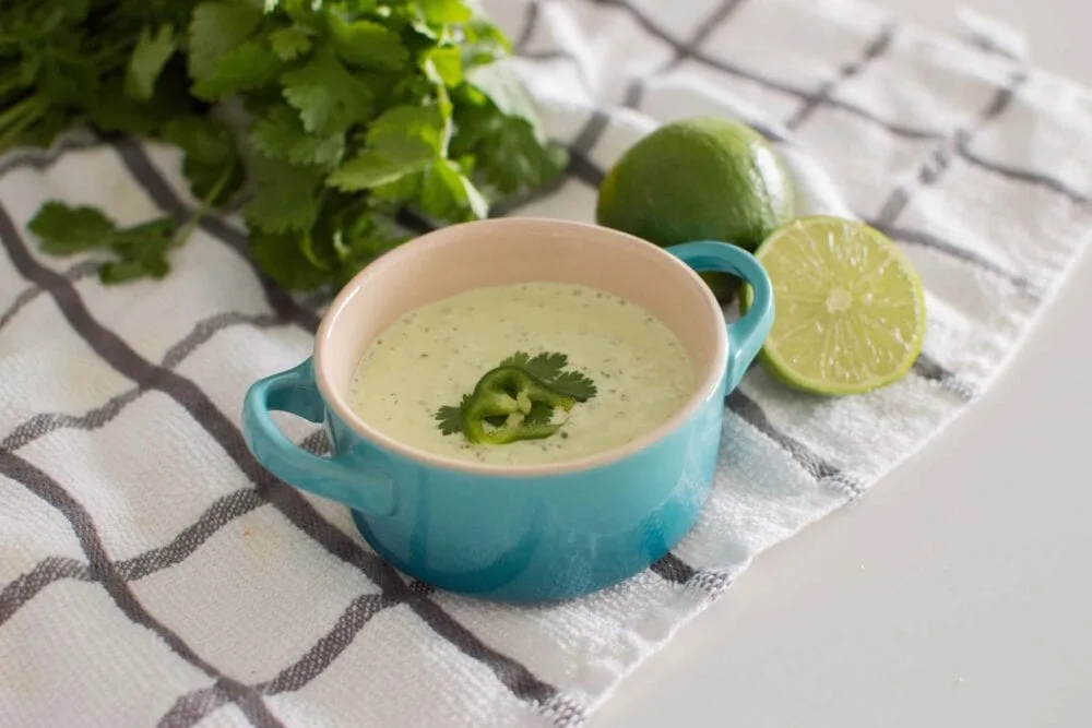Easy Jalapeno Aioli Recipe served in a blue serving dish, surrounded by limes and fresh cilantro