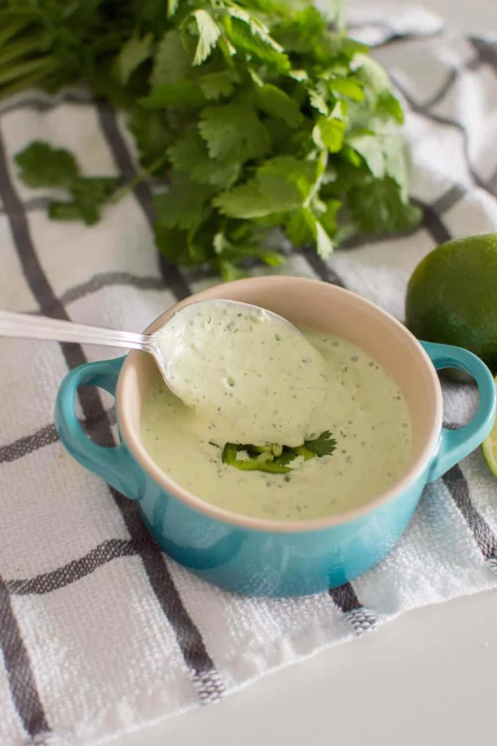 Easy Jalapeno Aioli Recipe served in a blue serving dish and being stirred with a spoon, surrounded by limes and fresh cilantro