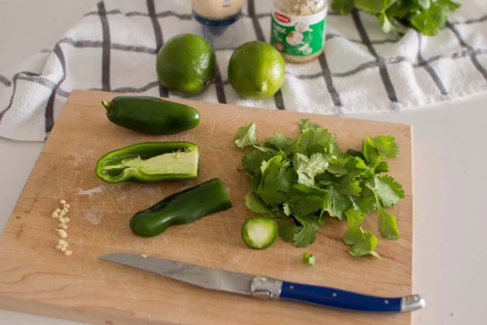 Cilantro and jalapenos being prepared and cut up on a wooden cutting board